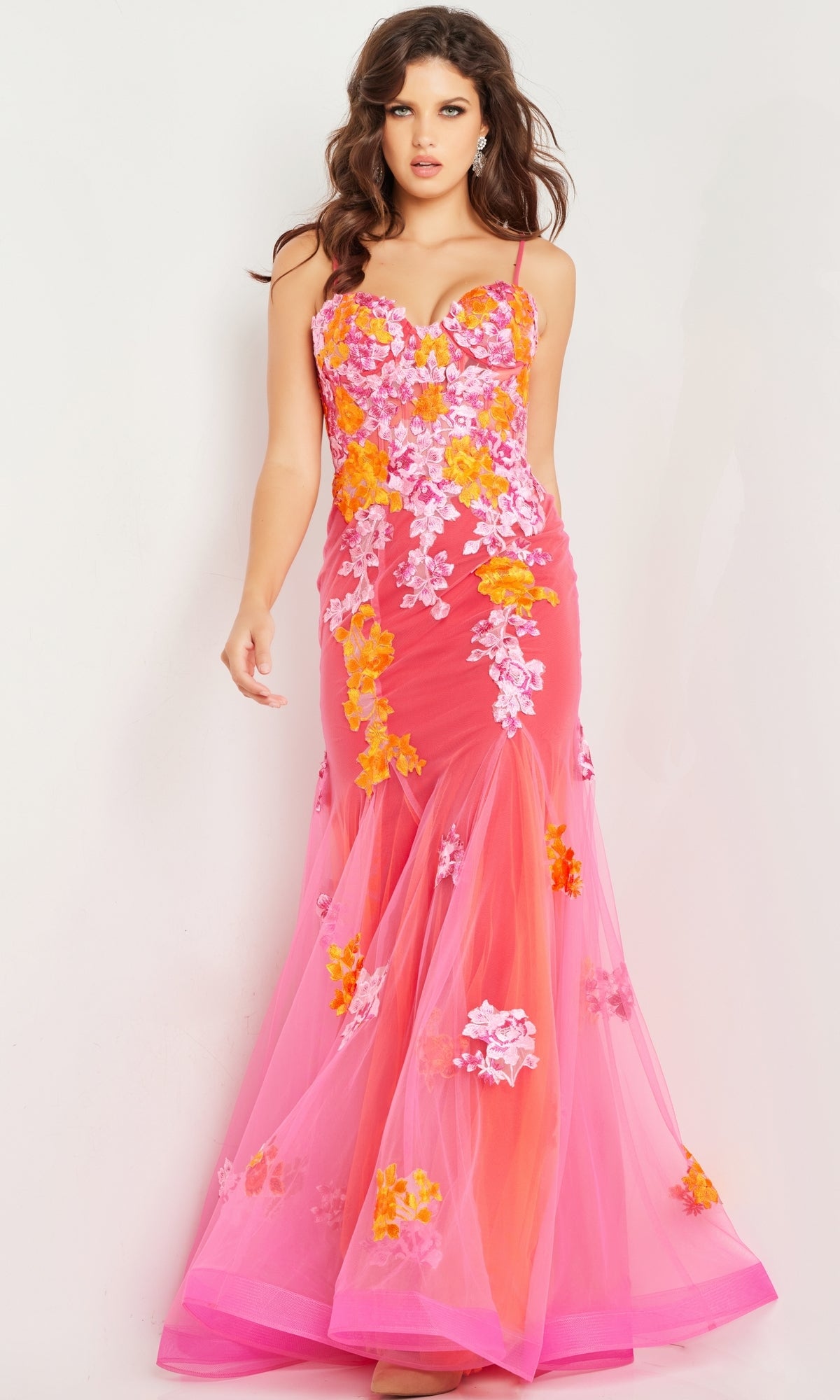 A woman wears the Long Prom Dress 36843 by Jovani—a fitted, floor-length pink mermaid tulle gown with orange and white floral embroidery, a sweetheart neckline, and a sheer overlay.